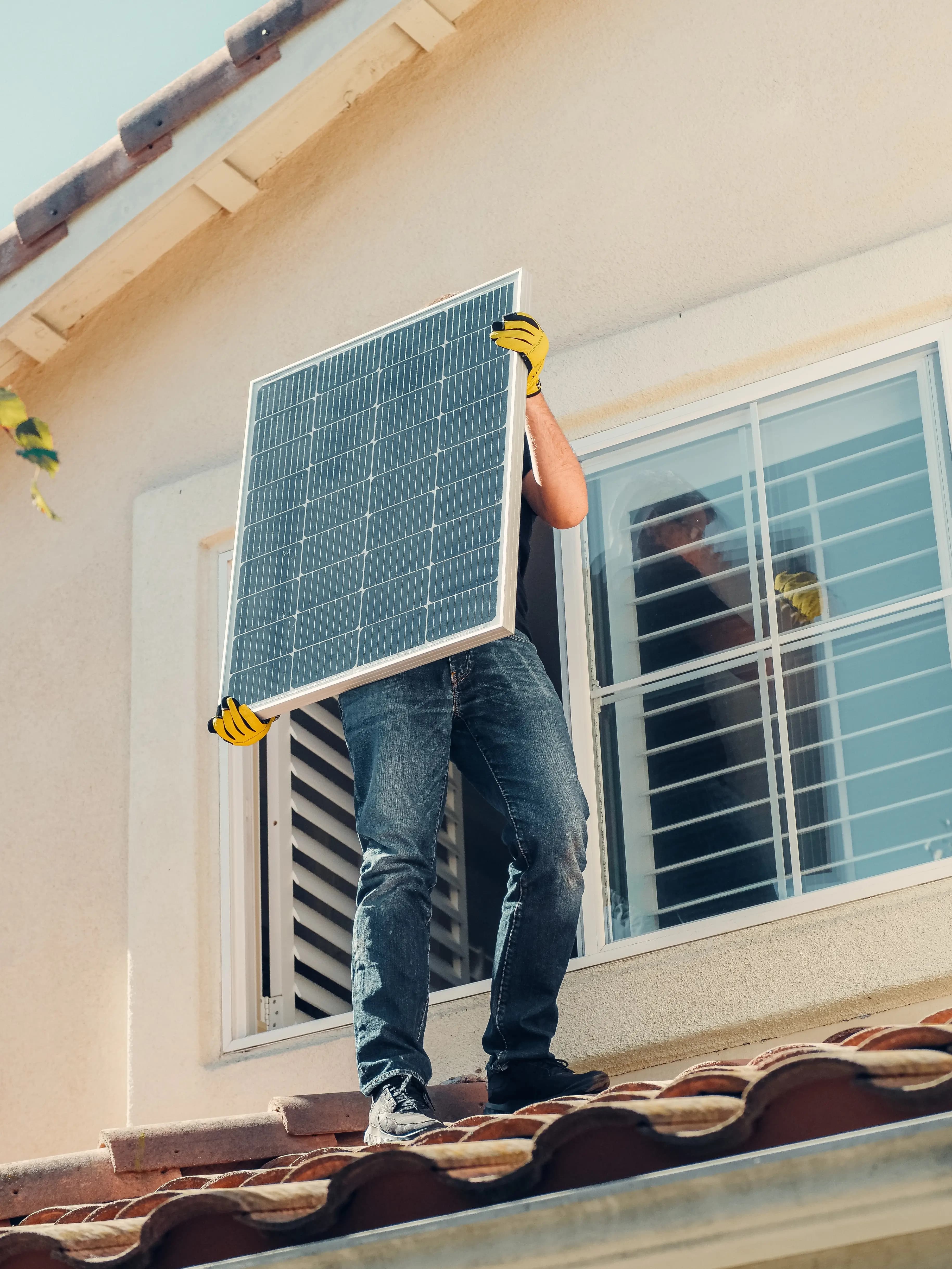 A man in a rooftop carrying a solar panel.